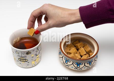 la mano di una donna mette un cubetto di zucchero in una tazza di tè. Foto di alta qualità Foto Stock