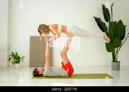 Un ragazzo in abbigliamento sportivo, si trova su un tappeto sportivo, lo yoga in coppia con una donna snella, facendo esercizi con supporto. Foto Stock