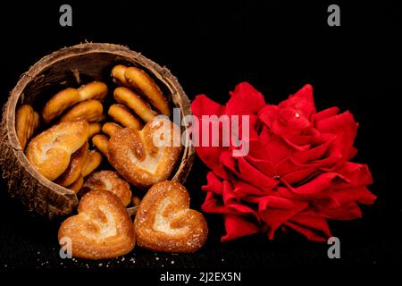 Biscotti a forma di cuore in conchiglia di cocco con rosa rossa, isolato con sfondo nero Foto Stock