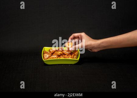 Cuori a forma di biscotto in Green Square Bowl, ragazza mano che raccoglie il biscotto, isolato su uno sfondo nero Foto Stock