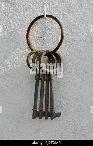 Vecchio mazzo di chiavi appese su una parete bianca Foto Stock