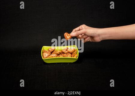 Cuori a forma di biscotto in Green Square Bowl, Boy Hand Pickup the Biscuit, isolato su sfondo nero Foto Stock