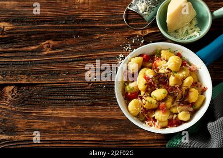 Vista dall'alto della padella con gustosi gnocchi di patate serviti con formaggio grattugiato e pomodori su un tavolo di legno per il pranzo Foto Stock