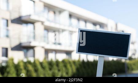 Cartellone nero vuoto contro la costruzione di un nuovo appartamento modello mockup vuoto etichetta Blackboard Casa in affitto. Appartamenti in vendita. Accedi davanti a nuovo Foto Stock