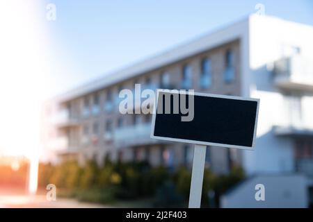 Cartellone nero vuoto contro la costruzione di un nuovo appartamento modello mockup vuoto etichetta Blackboard Casa in affitto. Appartamenti in vendita. Accedi davanti a nuovo Foto Stock