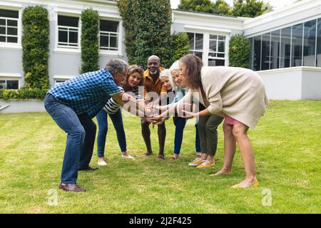 Multirazziale senior maschile e femminile amici impilare le mani mentre si gioca a rugby nel cortile Foto Stock