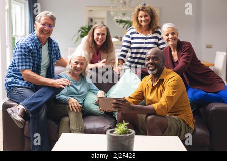 Ritratto di sorridenti amici senior multirazziali maschi e femmine sul divano a casa Foto Stock