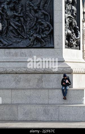 Un maschio soluto seduto sul plinth della colonna di Nelsons usando un telefono mobile Trafalgar Square Central London England UK Foto Stock