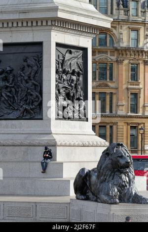 Un maschio soluto seduto sul plinth della colonna di Nelsons usando un telefono mobile Trafalgar Square Central London England UK Foto Stock