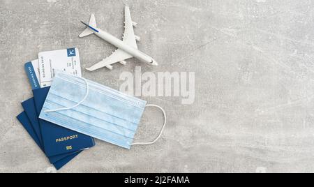 Concetto di viaggio e vacanza. Accessori e oggetti viaggio. Giocattolo dell'aeroplano sopra il passaporto con i biglietti dell'aeroplano e le maschere facciali. Vista dall'alto con disposizione piatta e copia Foto Stock