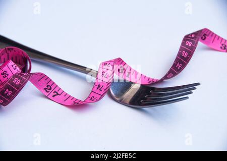 Nastro di misurazione con forcella su sfondo bianco. Perdita di peso e concetto di fitness Foto Stock