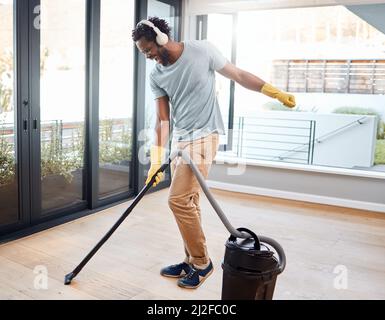 Il vuoto fa un buon sostituto per un compagno di ballo. Scatto di un giovane uomo che indossa le cuffie mentre aspira a casa. Foto Stock