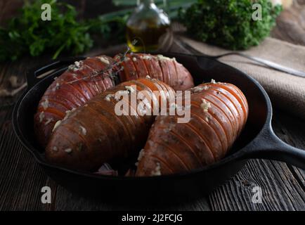 Patate dolci crude con erbe, aglio, sale e olio d'oliva. Pronto per cucinare. Servito su tavolo di legno scuro Foto Stock