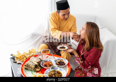 La giovane coppia musulmana celebra la fine del Ramadan, con il marito che mangia la moglie, simbolo dell'amore, con cucina tradizionale da un vassoio circolare Foto Stock