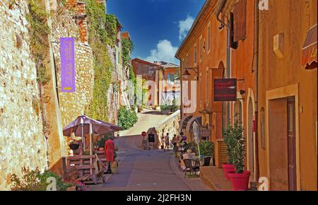 Roussillon en Provence, Francia - Ottobre 2. 2019: Vista su strada con muro di pietra naturale della fortezza e case mediterranee color ocra contro blu Foto Stock