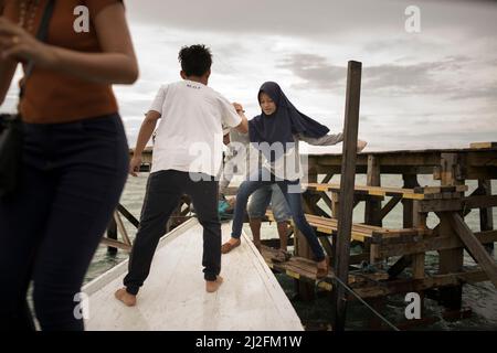 Un passeggero femminile di ferry boat salta da un molo a un ferry boat al largo della costa occidentale di Sulawesi, Indonesia, Asia. Foto Stock