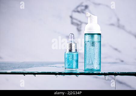 Bottiglia di siero o olio essenziale e lozione su ripiano di vetro in bagno con gocce d'acqua su sfondo di marmo. Cosmetica organica naturale. CENTRO BENESSERE, cura della pelle Foto Stock