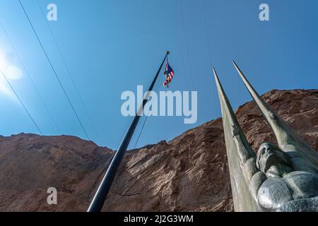 Un'inquadratura ad angolo basso della statua delle figure alate della Repubblica nella diga di Hoover con la bandiera degli Stati Uniti che galleggia Foto Stock