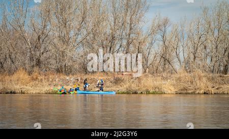 Evans, CO, USA - 26 marzo 2022: I pedalatori di kayak e canoe stanno atterrando su una riva per portarsi le barche sopra le dighe di diversione, all'inizio della primavera sul South Platt Foto Stock