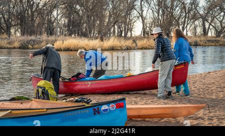 Evans, CO, USA - 26 marzo 2022: I pagaioli maschili e femminili stanno trasportando una canoa da lanciare per la prima gita primaverile in pagaiata sul fiume di South Platte in Foto Stock