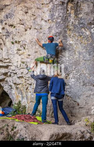 Il giovane si arrampica su una parete rocciosa in una grotta. Uomo che sale su una grande parete di pietra calcarea. Foto Stock