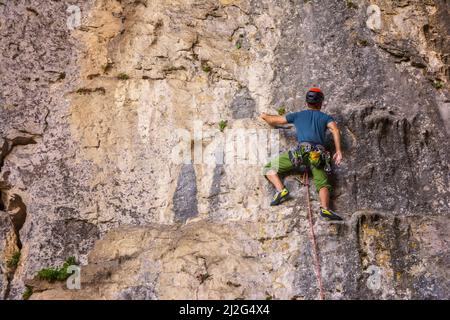 Il giovane si arrampica su una parete rocciosa in una grotta. Uomo che sale su una grande parete di pietra calcarea. Foto Stock