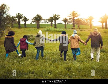 Le decisioni spontanee diventano avventure impressionanti. Foto retrostensiva di un gruppo di amici che camminano insieme in un campo. Foto Stock