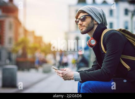 A chilometri di distanza, nel bel mezzo di tutto. Scatto di un giovane che usa il suo cellulare mentre fuori in città. Foto Stock