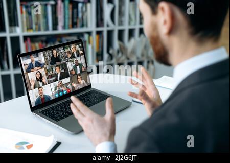 Formazione online, meeting a distanza. L'uomo d'affari caucasico, siede di fronte allo schermo del laptop in ufficio, conduce video riunione in linea con un gruppo internazionale di affari, spiega il concetto di funzionamento Foto Stock