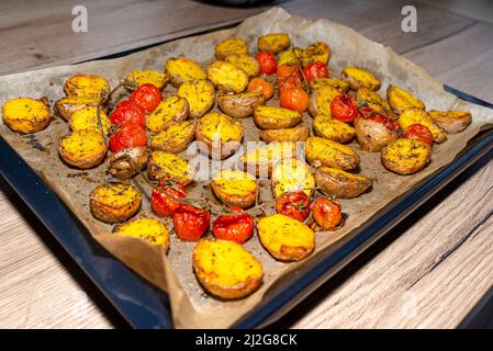 Patate al forno e pomodori ciliegini adagiati su una teglia da forno sul tavolo. Foto Stock
