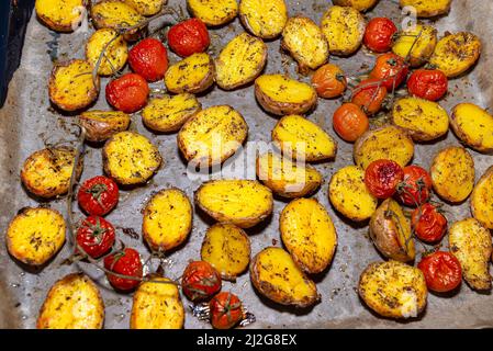 Patate al forno e pomodori ciliegini adagiati su una teglia da forno sul tavolo. Foto Stock