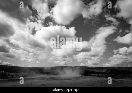 Un'immagine in scala di grigi di un geyser in Yellowstone sotto un cielo luminoso pieno di nuvole fluide Foto Stock