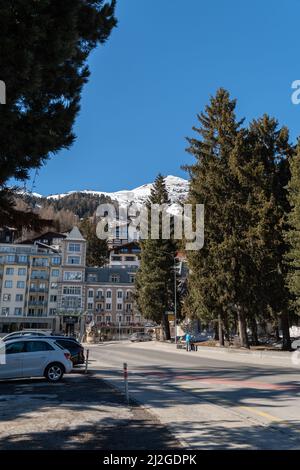 Davos, Svizzera, 23 marzo 2022 Vista su una strada e un piccolo parco con alberi e alcuni edifici sullo sfondo in una giornata di sole Foto Stock