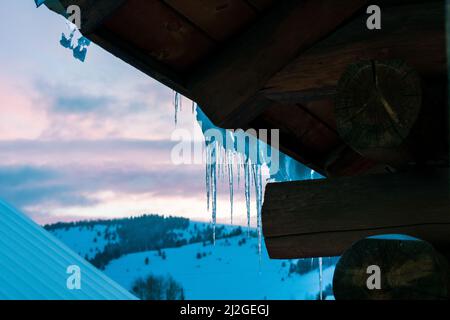 Ghiaccioli sul tetto contro un tramonto rosa Foto Stock