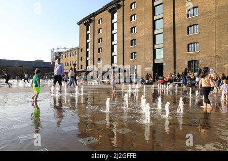 I bambini giocano al sole primaverile nelle fontane di Granary Square, a Kings Cross, a nord di Londra, Regno Unito Foto Stock