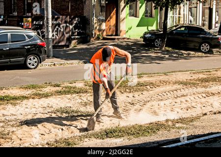 Dnepropetrovsk, Ucraina - 09.15.2021: Un lavoratore con una pala in uniforme arancione pulisce le rotaie del tram dai detriti di costruzione. Foto Stock