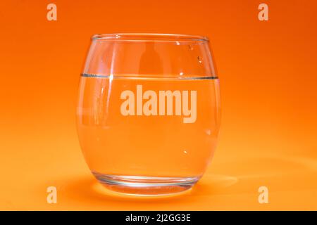 Bicchiere di vetro con acqua purificata su sfondo arancione e arancione chiaro. Spazio di copia Foto Stock