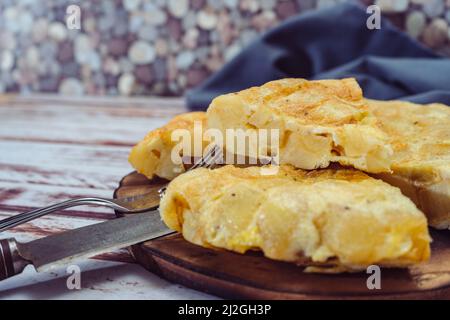 Vista normale di un piatto con una frittata di patate spagnola tagliata in ottanta su un tavolo di legno. Cibo tradizionale. Foto Stock