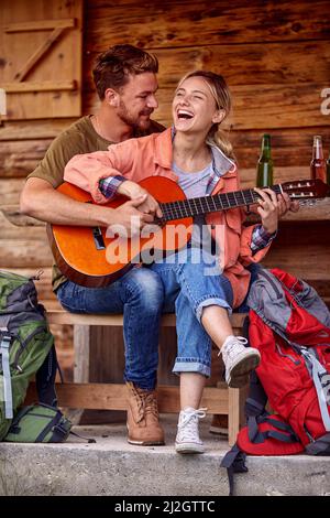 Una giovane coppia ama suonare una chitarra al portico del cottage insieme in una bella serata. Vacanza, rapporto, cottage Foto Stock