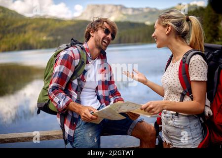 Una giovane coppia che si riposa accanto al lago e utilizza una mappa per fare un piano escursionistico in una bella giornata. Viaggio, natura, escursioni Foto Stock