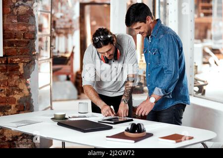 Un altro giorno occupato sul lavoro. Scatto corto di due giovani uomini d'affari che lavorano insieme in un ufficio all'interno del loro laboratorio. Foto Stock