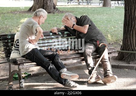 SOFIA, BULGARIA - 02 AGOSTO 2017: Due uomini di mezza età seduti su una panchina e giocando una partita di scacchi in un giardino della città di Sofia centro Foto Stock