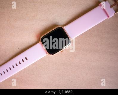 Orologio wireless Smart con cinturino rosa isolato su sfondo marrone in carta kraft. Foto Stock