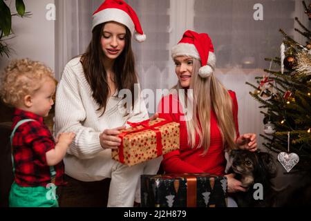 Regalare un bambino di due anni. Madre e figlia sono seduti accanto al loro fratello. Foto Stock