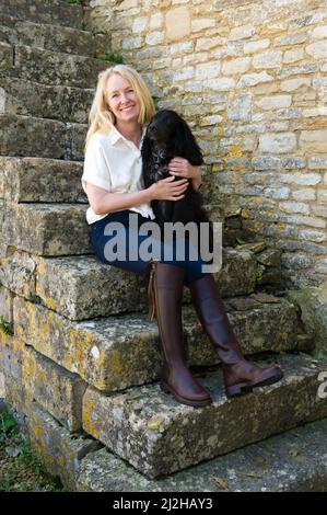 Ritratto di donna sorridente seduta su gradini di pietra con cane Foto Stock