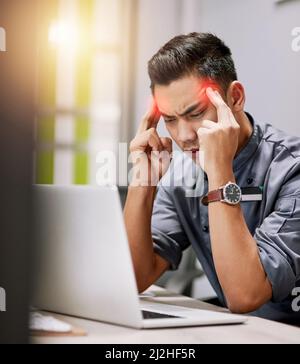 La pressione sta arrivando a lui. Scatto di un giovane che soffre di mal di testa mentre lavora sul suo laptop. Foto Stock