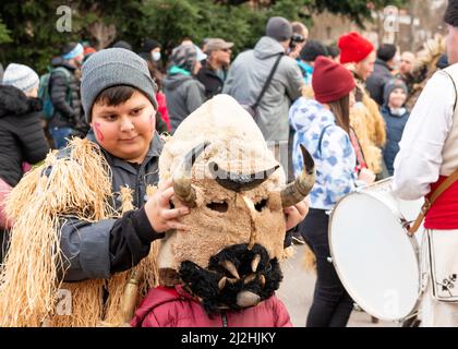 Ragazzo bulgaro al festival mistico tradizionale del millennio di Kukeri a Sofia, Bulgaria, Balcani, Europa orientale. Kukeri è una tradizione secolare volta a cacciare gli spiriti malvagi e a invitare il bene, tenuto intorno all'inizio dell'inverno o a metà dell'inverno. I partecipanti indossano campane sovradimensionate, costumi ricamati e maschere fantastiche per partecipare al rituale invernale. Foto Stock