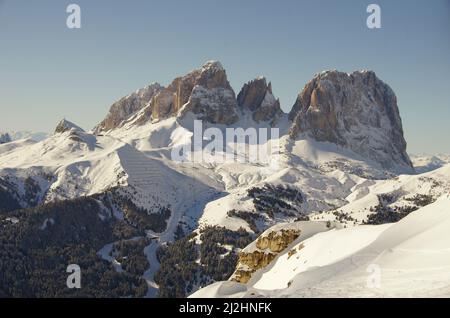 Enormi rocce di montagna dolomitica, che si innalzano sopra la neve, con una valle innevata, gli sci e gli alberi sottostanti Foto Stock