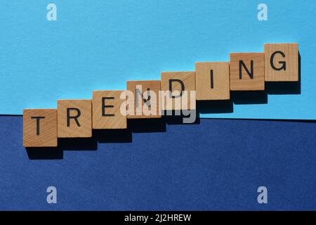 Tendenza, parola in lettere di legno alfabeto isolato su sfondo blu Foto Stock