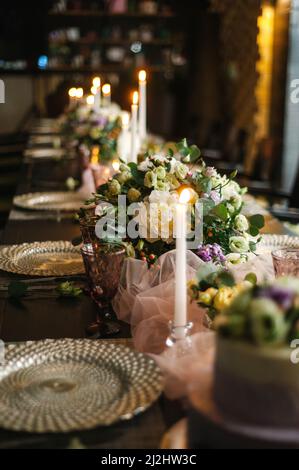 Elegante banchetto con piatti d'argento, fiori teneri e candele al tavolo servito in un ristorante. Festa serale, festa. Foto Stock